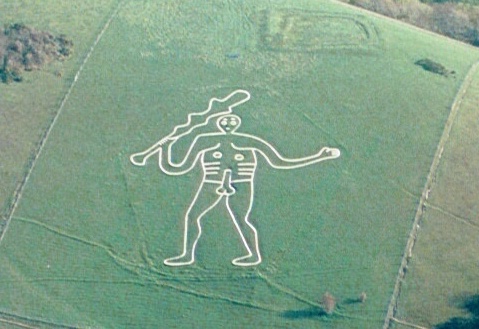 A zoomed-in image of the Cerne Abbas Hill Giant in Dorset, England. The giant figure is holding a large club and has an erect phallus. The giant seems to be gesturing toward the viewer.
